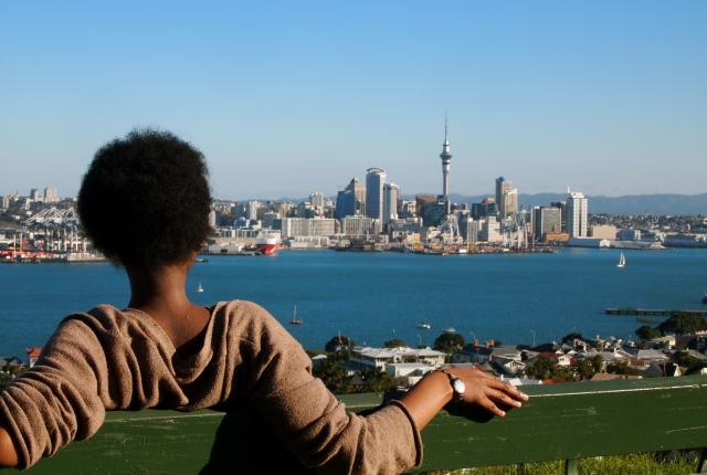 a student sitting on a bench at the top of Mount Victoria, looking at the Auckland skyline